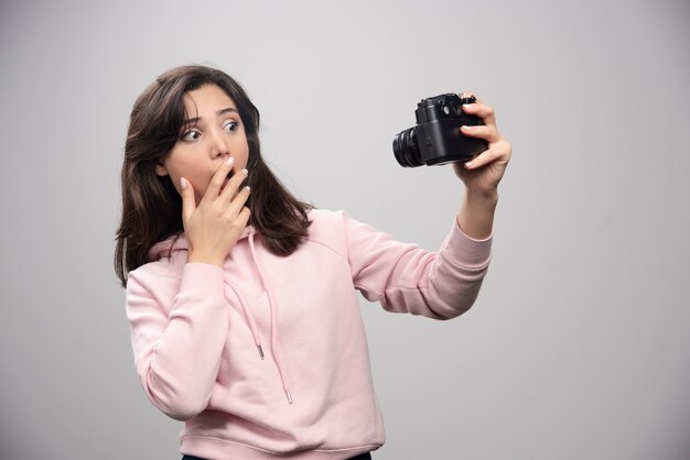 Fotograf kobieta robi selfie na szarej ścianie.