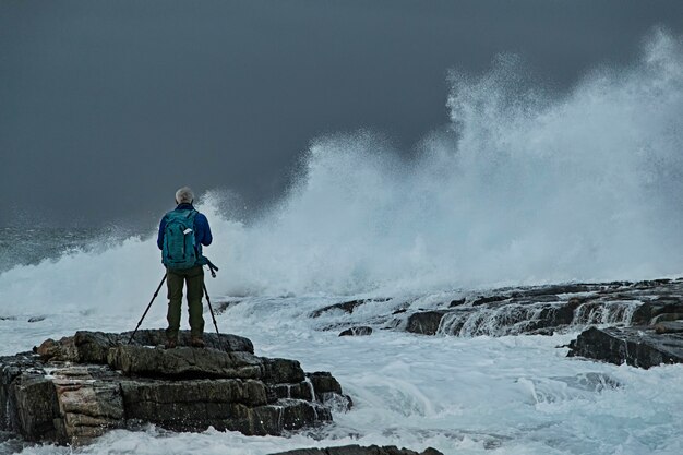 fotograf na skałach w wzburzonym morzu