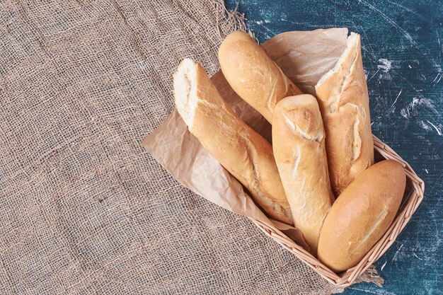 Francuskie bagietki w koszu na niebieskim stole.