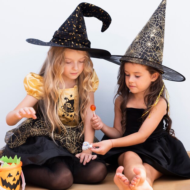 Frontowego widoku małe dziewczynki siedzi na podłoga na Halloween