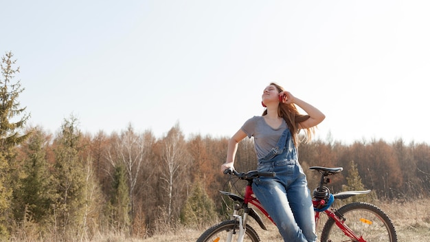 Frontowy widok beztroska kobieta z hełmofonami na bicyklu w naturze