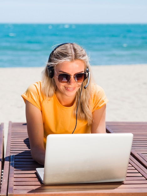 Frontowy widok kobieta z słuchawki i laptopem pracuje przy plażą