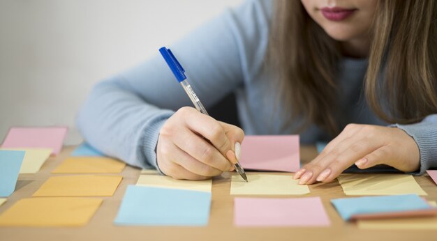 Frontowy widok kobiety writing na kleistych notatkach przy biurem