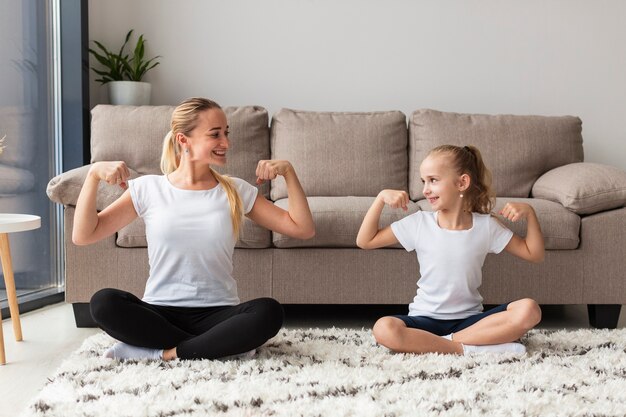 Frontowy widok matka i córka pokazuje daleko bicepsy w domu