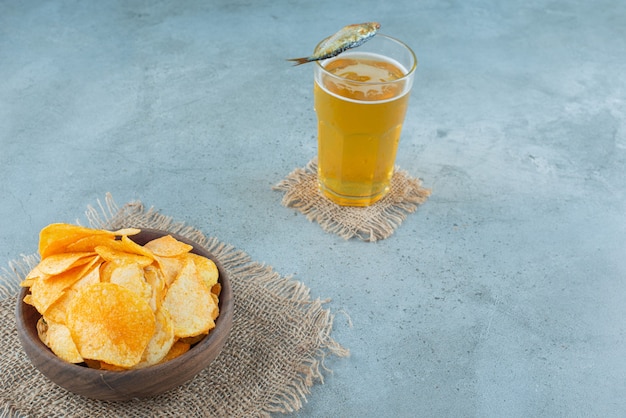Frytki w misce obok szklanki piwa, na marmurowym stole.
