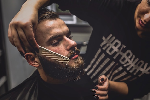 Fryzjer przeczesuje brodę stylowego mężczyzny
