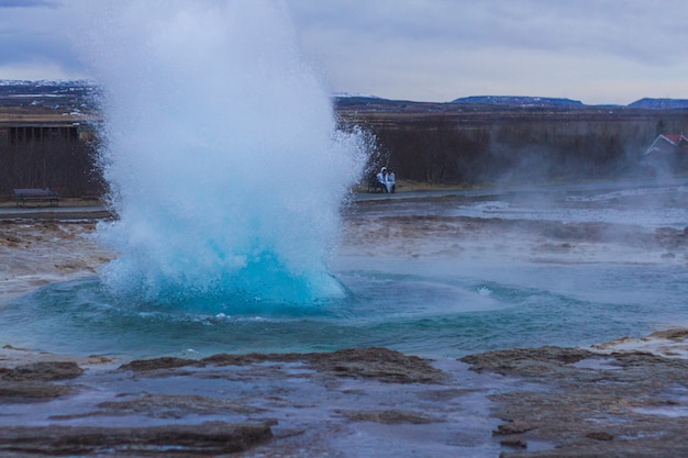 Bezpłatne zdjęcie gejzer strokkur otoczony wzgórzami pod zachmurzonym niebem wieczorem na islandii