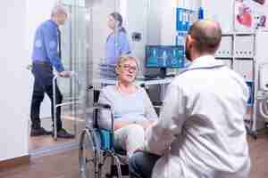 Bezpłatne zdjęcie giatra konsultujący inwalidę na wózku inwalidzkim w szpitalnej sali egzaminacyjnej