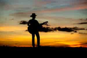 Bezpłatne zdjęcie gitarzysta dziewczyna sylwetka na zachód słońca