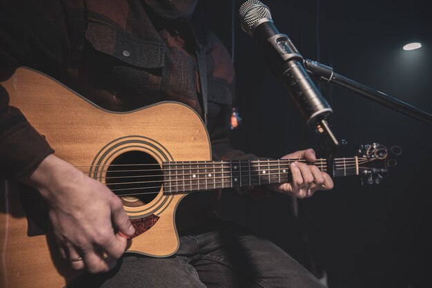 Gitarzysta gra na gitarze akustycznej z kapodasterem przed mikrofonem