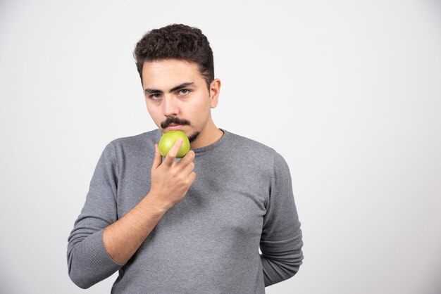 Głodny mężczyzna trzyma zielone jabłko i wygląda poważnie.
