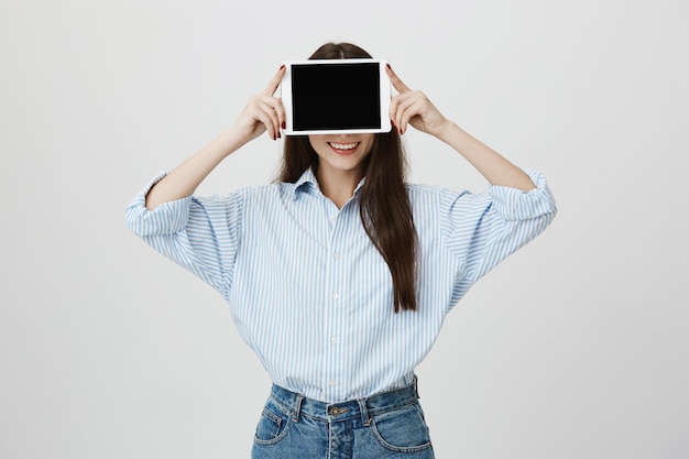 Bezpłatne zdjęcie głupia kobieta pokazująca język i zakrywająca oczy cyfrowym tabletem