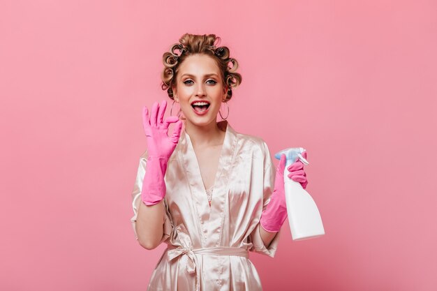 Gospodyni domowa w różowych rękawiczkach trzyma środek do mycia okien i pokazuje znak OK