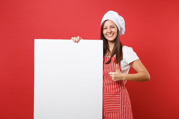 Gospodyni kobieta kucharz kucharz piekarz w pasiasty fartuch, biała koszulka, kapelusz kucharzy toczek na białym tle na czerwonym tle. kobieta trzyma duży biały pusty billboard dla treści promocyjnych. makieta koncepcja przestrzeni kopii.