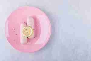 Bezpłatne zdjęcie gotowane kiełbaski ozdobione cytryną na różowym talerzu.k