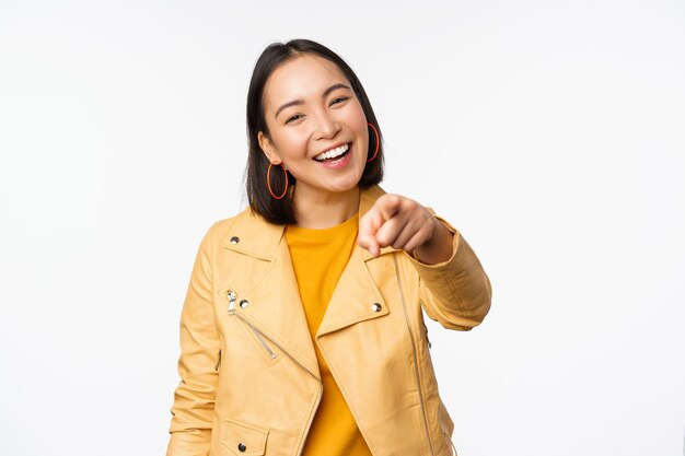 Gratulacje to ty Szczęśliwa piękna azjatycka kobieta śmiejąca się wskazującym palcem na kamerę wybierająca zapraszanie ludzi rekrutujących stojących na białym tle