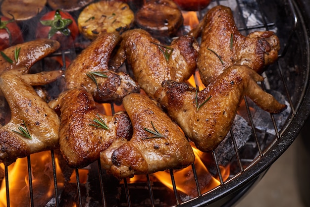 Grillowane skrzydełka z kurczaka na płonącym grillu z grillowanymi warzywami w sosie barbecue z pieprzem rozmarynem, solą.