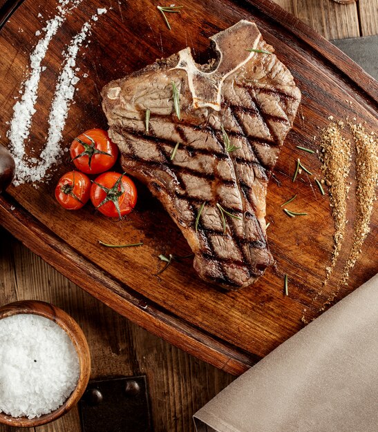 Grillowany stek t-bone podawany z ziołowymi solami i grillowanymi pomidorami cherry