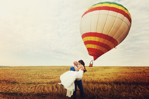 Groom trzyma panny młodej w ramionach, podczas gdy wiatr wieje balon powietrza