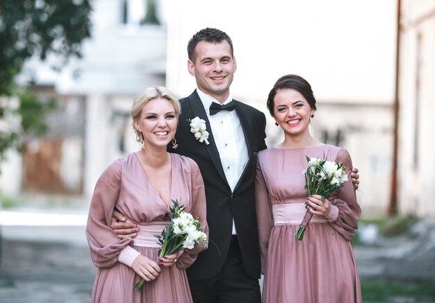 Bezpłatne zdjęcie groomsman obejmuj? c dwie sta? e druhna stoj? cych na zewn? trz