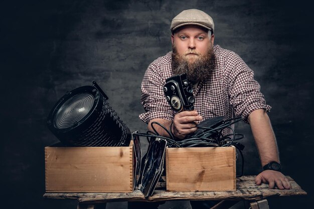 Gruby, brodaty mężczyzna hipster trzyma w ręku kamerę wideo 8 mm i kolorowe lampy w podsufitkach.