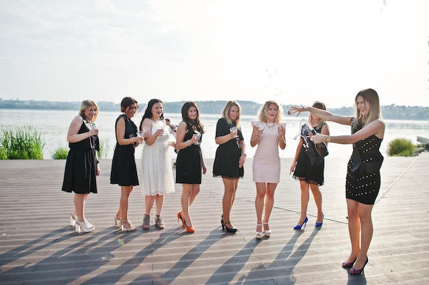 Grupa 8 dziewczyn ubiera się na czarno i 2 panny młode na wieczorze panieńskim przed słoneczną plażą pijąc szampana
