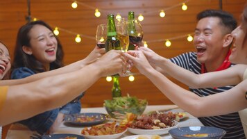 Grupa azjatyckich ludzi pijących alkohol wiwatuje butelkę piwa i jedząc jedzenie siedząc przy stole