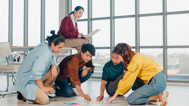 Grupa azjatyckich młodych kreatywnych ludzi w codziennym stroju omawiająca pomysły na spotkania biznesowe podczas burzy mózgów, plan projektu projektowania aplikacji mobilnych, rozłożony na piętrze w biurze. Koncepcja pracy zespołowej współpracownika.