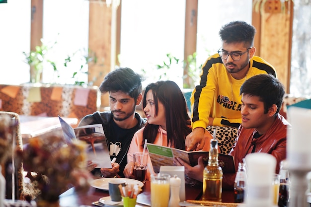 Grupa azjatyckich przyjaciół siedzących w kawiarni Szczęśliwi Hindusi bawią się razem siedząc na kanapie i wybierają posiłki z menu