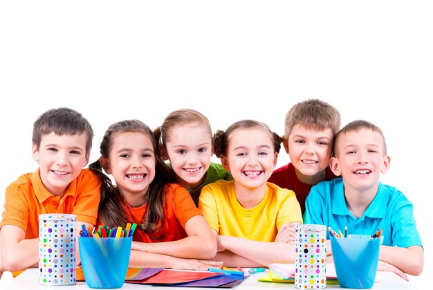 Grupa dzieci siedzi przy stole z markerami, kredkami i kolorowym kartonem.