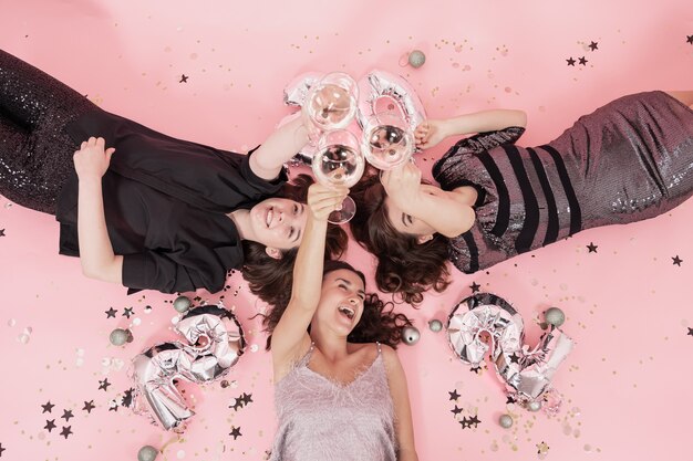 Grupa dziewczyn bawiących się na przyjęciu bożonarodzeniowym leżącym na różowym tle z kieliszkami szampana, nowy rok 2022.