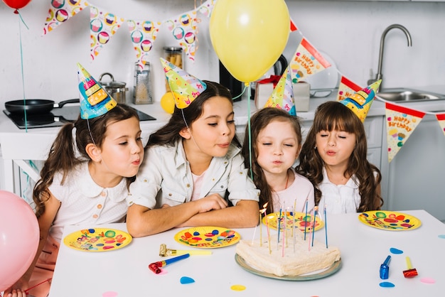 Grupa dziewczyny dmucha świeczki na urodzinowym torcie