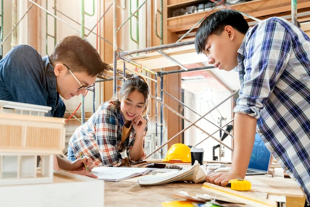 Grupa inteligentnych azjatyckich architektów zajmujących się projektowaniem wnętrz, konsultacjami z inżynierem constrction, spotkanie podczas spotkania z projektem domu i makieta domu w tle struktury remontu domu