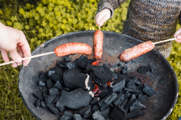 Grupa ludzi przygotowywa kiełbasy na przenośnym grillu