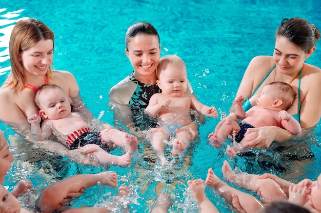 Grupa matek z małymi dziećmi na dziecięcej lekcji pływania z trenerem.