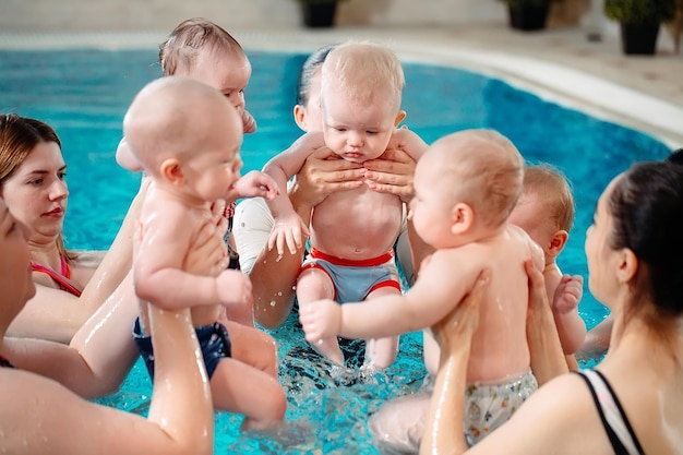 Grupa matek z małymi dziećmi na dziecięcej lekcji pływania z trenerem.