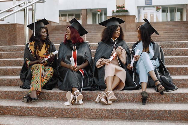 Grupa młodych afro amerykańskich studentek ubranych w czarną suknię ukończenia szkoły. kampus jako tło