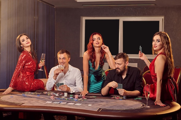 Grupa młodych graczy pozuje przy stole pokerowym w kasynie i patrzy w kamerę. Młodzi stawiają zakłady, czekając na wielką wygraną. Hazard za pieniądze. Gry losowe.