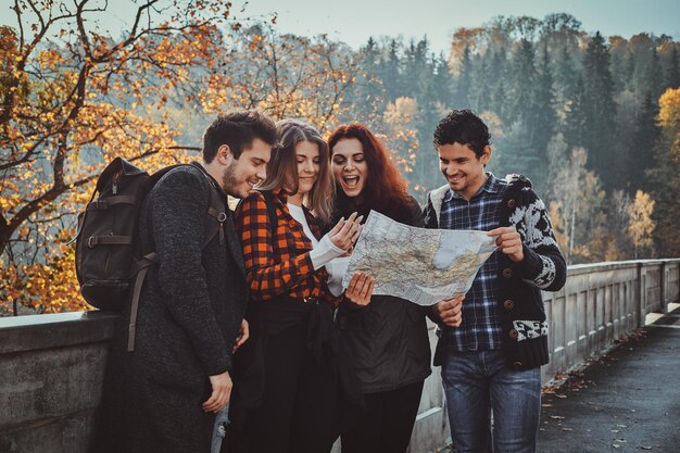 Grupa młodych ludzi patrzy na mapę, na której się znajduje, spacerując po jesiennym lesie.