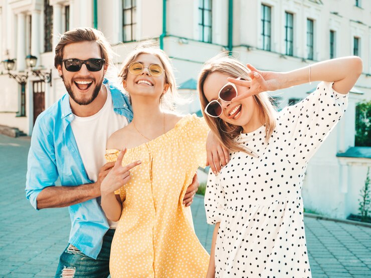 Bezpłatny plik Zdjęcie grupa młodych trzech stylowych przyjaciół pozowanie na ulicy. moda mężczyzna i dwie słodkie dziewczyny ubrane w letnie ubrania. uśmiechnięte modele zabawy w okularach przeciwsłonecznych. wspaniałe kobiety i facet w susnet