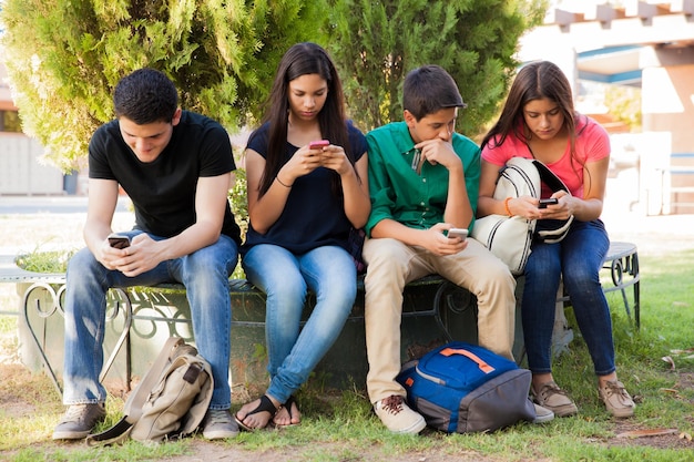 Grupa nastoletnich chłopców i dziewcząt ignorujących się nawzajem podczas korzystania z telefonów komórkowych w szkole