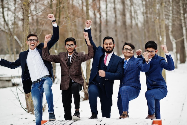 Grupa pięciu indyjskich biznesmenów w garniturach pozowanych na zewnątrz w zimowy dzień w Europie ręce do góry i okazują szczęśliwe emocje