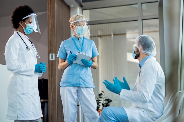Grupa pracowników służby zdrowia rozmawiająca w szpitalnym korytarzu podczas pracy podczas pandemii koronawirusa