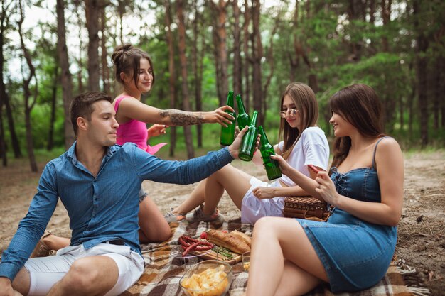 Grupa przyjaciół brzęk butelek piwa podczas pikniku w lesie latem