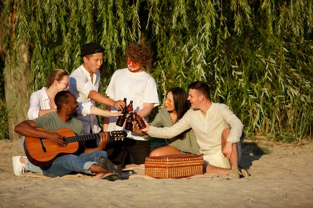 Grupa przyjaciół stukająca się szklankami piwa podczas pikniku na plaży?