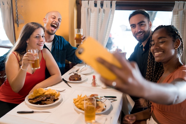 Grupa Różnorodnych Przyjaciół Robi Selfie Telefonem Komórkowym Podczas Wspólnego Posiłku W Restauracji. Koncepcja Przyjaciół.