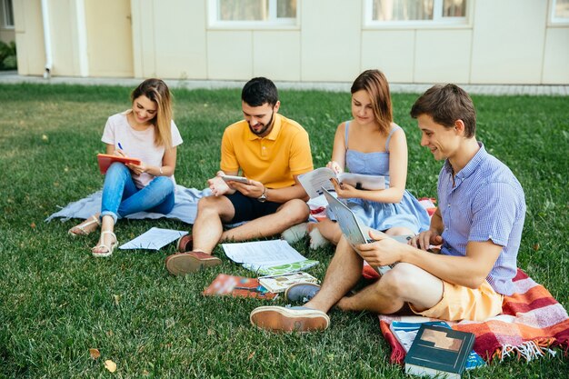 Grupa studiowania ucznie siedzi na trawie z nutowymi książkami