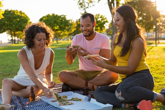 Grupa szczęśliwi zamknięci przyjaciele je pizzę w parku