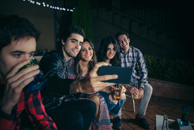 Grupa szczęśliwych młodych przyjaciół picia i robienia zdjęć selfie z smartphone na imprezie na świeżym powietrzu. koncepcja przyjaźni i uroczystości.