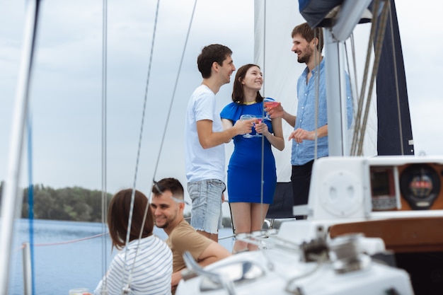 Bezpłatne zdjęcie grupa szczęśliwych przyjaciół pijących koktajle wódki na imprezie na łodzi na świeżym powietrzu, lato